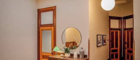 A hallway with a wooden cabinet, a mirror, a hanging light fixture, and a door leading to another room.