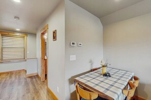 A room with a wooden floor, a checkered table, and a window with blinds. - 4BR home with hot tub, fast wifi, & full kitchen (Ronald)