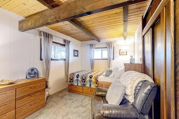 Ein Schlafzimmer mit Holzboden, einem Bett mit gemustertem Überwurf, einem Ledersofa, einer Holzkommode und einem Ventilator.