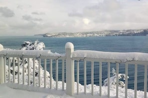 Ein mit Schnee bedeckter Balkon mit Blick auf ruhiges Wasser und eine ferne Küstenlinie.