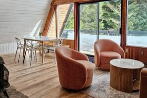 A modern interior with a wooden floor, a dining table with chairs, and two cushioned seating areas. - Modern A-frame 2BR near lake & lifts with firepit (Snoqualmie Pass)