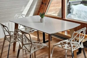 A dining area with a white table, white chairs with geometric patterns, and a small potted plant. - Modern A-frame 2BR near lake & lifts with firepit (Snoqualmie Pass)