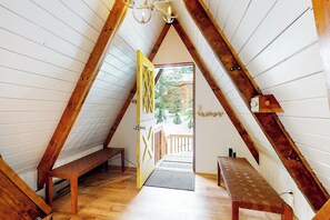 A room with a sloped ceiling, wooden beams, a bench, a door with a geometric pattern, and a small table. - Modern A-frame 2BR near lake & lifts with firepit (Snoqualmie Pass)