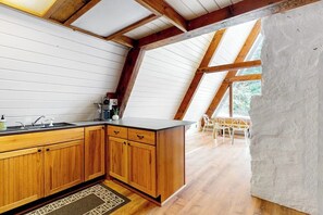 A kitchen with wooden cabinets, a black countertop, and a window overlooking a dining area. - Modern A-frame 2BR near lake & lifts with firepit (Snoqualmie Pass)