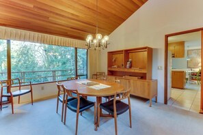 A dining area with a wooden table and chairs, a chandelier, and a view of trees through large windows. - Stylish 3BR - Fireplace - Deck - Washer Dryer (Port Angeles)