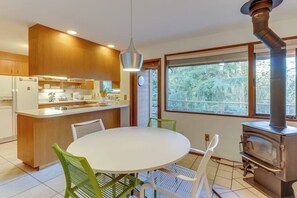 A modern kitchen with a central island, a dining table with chairs, and a wood-burning stove. - Stylish 3BR - Fireplace - Deck - Washer Dryer (Port Angeles)