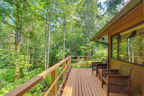 A wooden deck with a railing, surrounded by dense forest. - Stylish 3BR - Fireplace - Deck - Washer Dryer (Port Angeles)