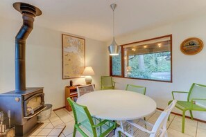 A room with a round table, green chairs, a map on the wall, a window with a view, and a wood-burning stove. - Stylish 3BR - Fireplace - Deck - Washer Dryer (Port Angeles)