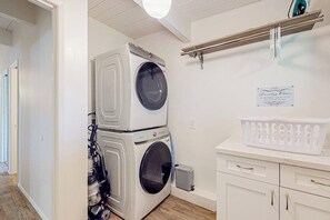 A laundry room with stacked washers and dryers, a drying rack, and a basket on a counter. - 3BR bay-front dog-friendly home, modern interior (Gig Harbor)