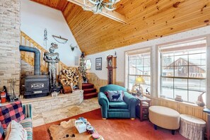 A cozy living room with a fireplace, a sofa, a chair, and a window with a view of a wooden cabin. - 2BR cabin with balcony, grill, & Washer Dryer (Cle Elum)