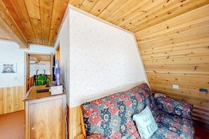 A room with a wooden ceiling, a bed with patterned bedding, a bedside table with a lamp, and a green bag on the floor. - 2BR cabin with balcony, grill, & Washer Dryer (Cle Elum)