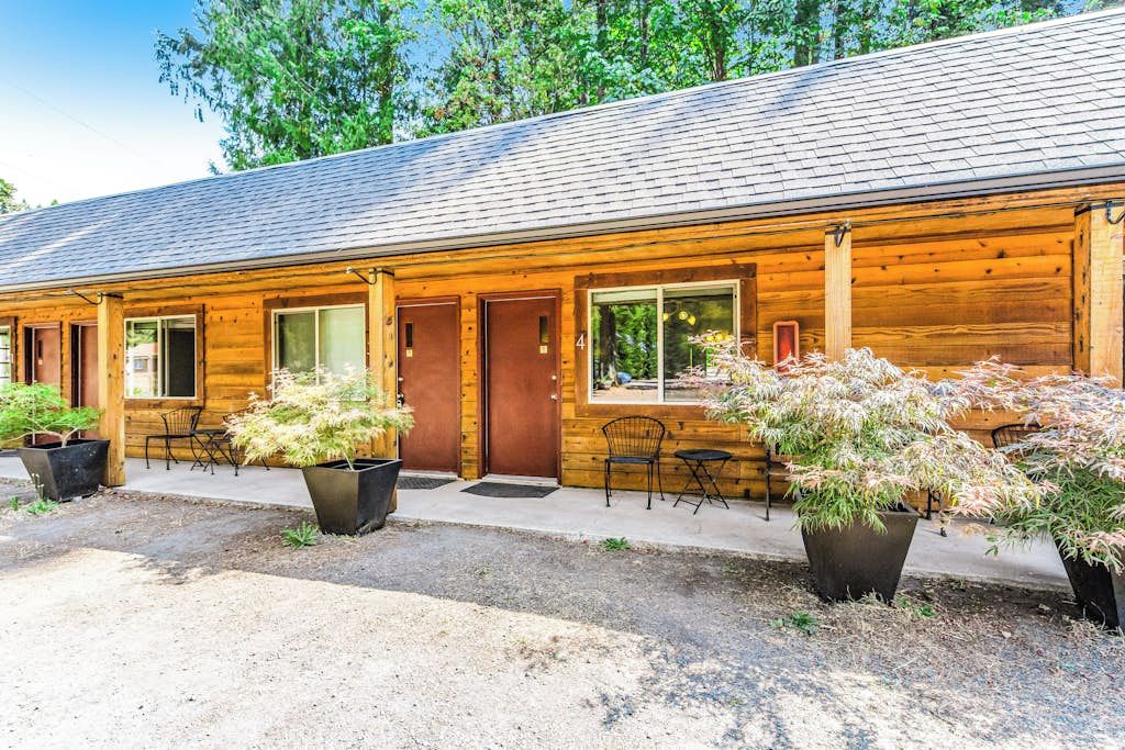 A wooden building with a sloped roof, multiple windows, and doors. There are potted plants and outdoor seating.