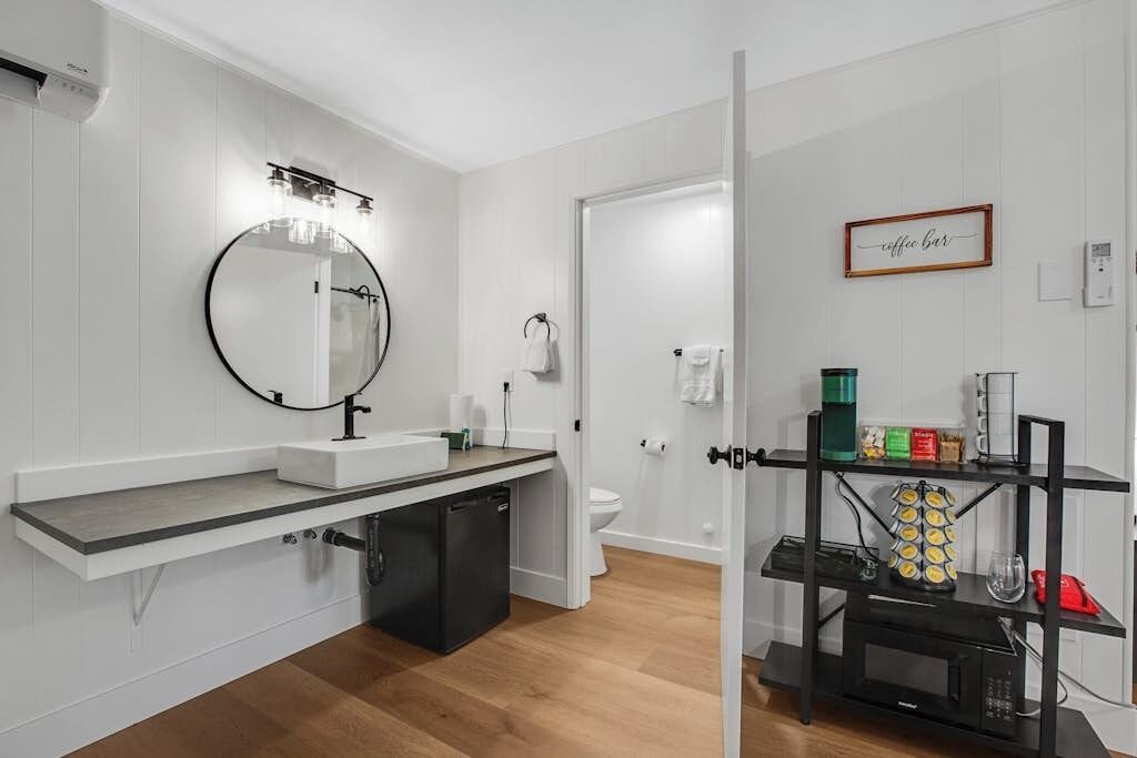 Une salle de bain moderne avec un grand miroir rond, un lavabo blanc, des toilettes et un coin café.