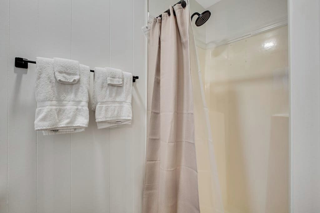 A bathroom with two white towels hanging on a black towel bar, a beige shower curtain, and a white bathtub.