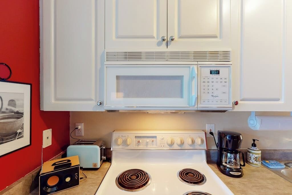 A kitchen with white cabinets, a microwave, a stove, a toaster, and a coffee maker.