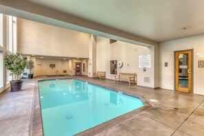 Une piscine intérieure avec un sol carrelé, des bancs et des plantes en pot.