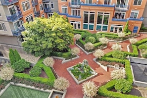 A multi-story residential building with balconies, a central courtyard with geometric landscaping, and a large tree.