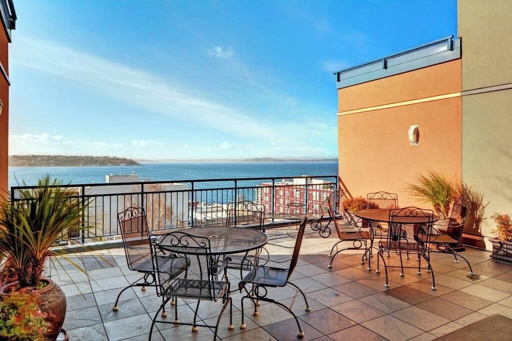 Une terrasse avec mobilier d’extérieur, une vue sur la mer et un bâtiment doté d’un balcon.