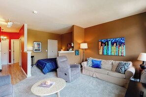 Une chambre d’hôtel avec un lit, un canapé, une chaise, une petite table et un tableau au mur.