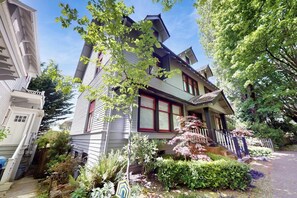 Une maison à deux étages avec un porche à l’avant, entourée d’une végétation luxuriante et d’un petit jardin.