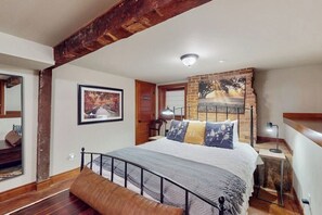 Une chambre à coucher avec un lit, un banc en bois, un mur en briques et un tableau encadré.