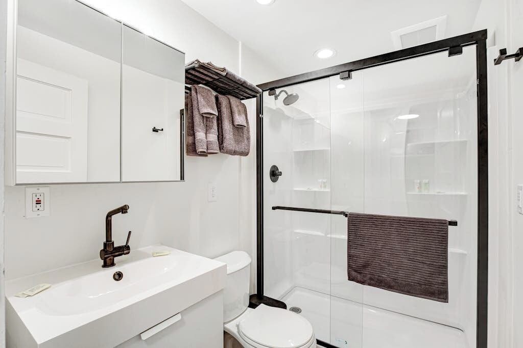 A modern bathroom with a white sink, a toilet, a glass-enclosed shower, and a mirror above the sink.