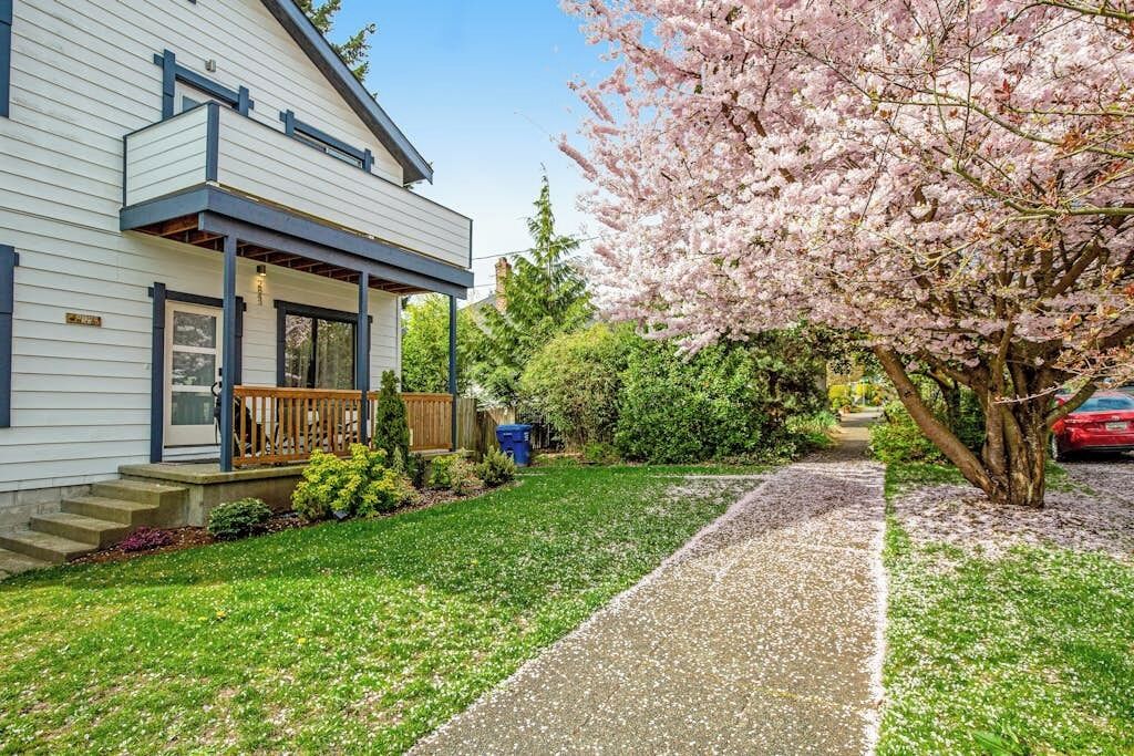 A two-story house with a covered porch, a well-maintained lawn, and a cherry blossom tree.