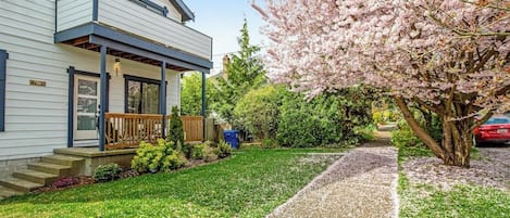 A two-story house with a covered porch, a well-maintained lawn, and a cherry blossom tree.