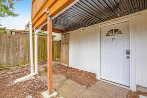 Un espacio exterior techado con una puerta blanca, cerca de madera y estructura de techo metálico.