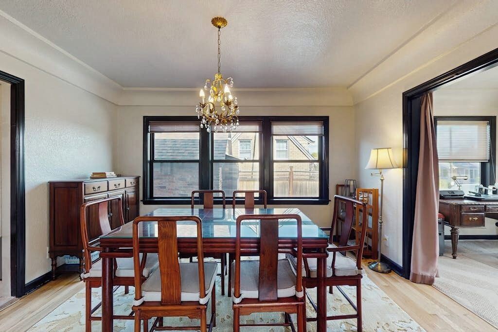 A dining area with a large table and chairs, a chandelier, and a view through the window.