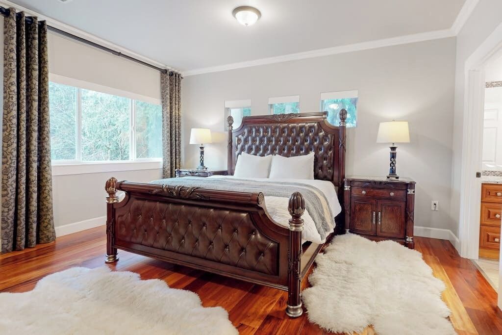 Une chambre à coucher avec un grand lit, deux tables de chevet, une commode et une fenêtre avec des rideaux.