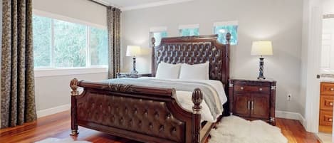 Une chambre à coucher avec un grand lit, deux tables de chevet, une commode et une fenêtre avec des rideaux.
