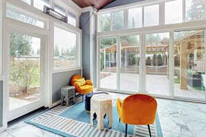 Une pièce lumineuse, baignée de soleil, avec de grandes fenêtres, un fauteuil jaune, un pouf à motifs et un tapis rayé.