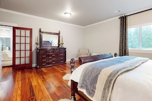 Une chambre avec un plancher en bois, un lit recouvert d’une couverture à rayures, une commode avec un miroir et une fenêtre avec des rideaux.