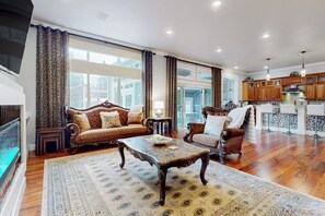 A spacious living room with a fireplace, a large window, and a kitchen area with wooden cabinets.