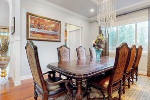 A dining room with a large wooden table, ornate chairs, a chandelier, and a framed artwork on the wall.