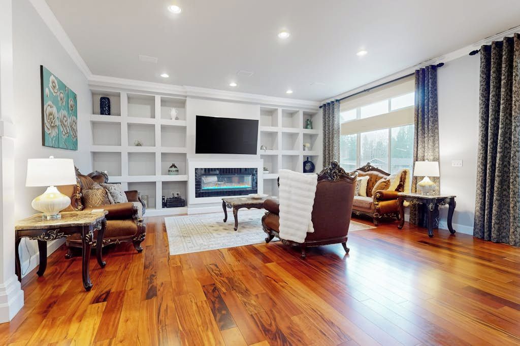 A spacious living room with a fireplace, wooden flooring, and a large TV mounted on the wall.
