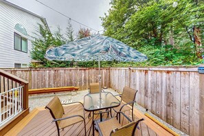 A deck with a table and chairs, an umbrella, and a wooden fence. - Modern 1BR with fireplace & inviting patio (Woodinville)