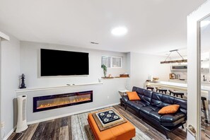 A modern living room with a fireplace, a black leather sofa, and a flat-screen TV mounted on the wall. - Modern 1BR with fireplace & inviting patio (Woodinville)