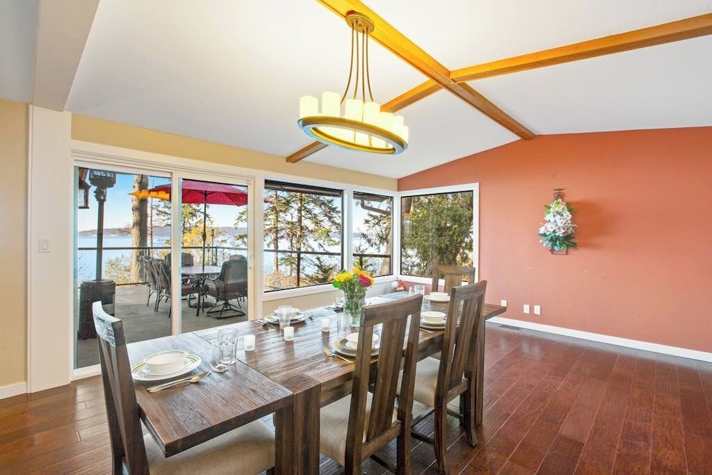 Zona pranzo con tavolo di legno apparecchiata per quattro persone, ampie finestre e ventilatore a soffitto.