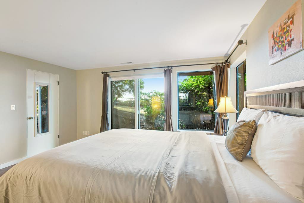 A hotel room with a large bed, a nightstand with a lamp, and a view through the window.