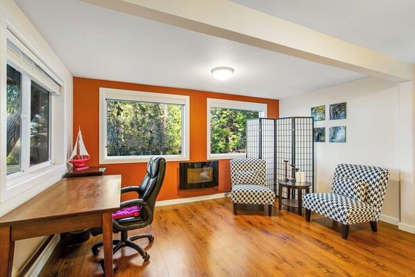 A room with a wooden floor, a fireplace, a dining table, and two patterned armchairs.