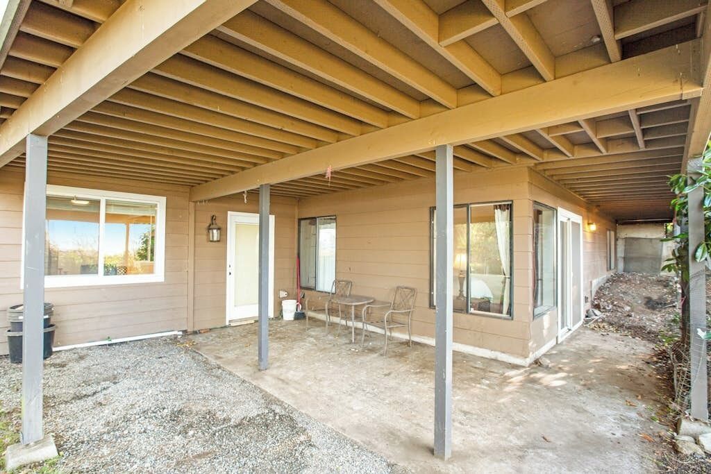 A covered outdoor area with a patio, a table with chairs, and a door leading to the building.