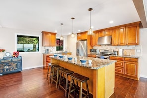 A modern kitchen with wooden cabinets, a central island with stools, and stainless steel appliances.