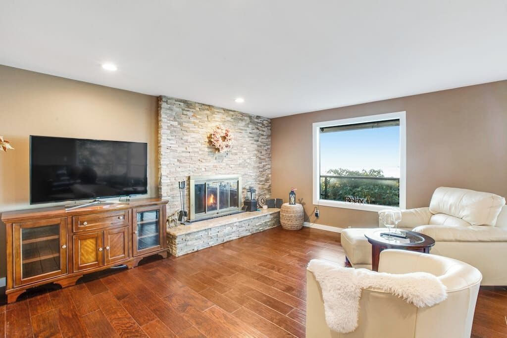 A living room with a stone fireplace, a flat-screen TV, a leather sofa, and a large window with a view.