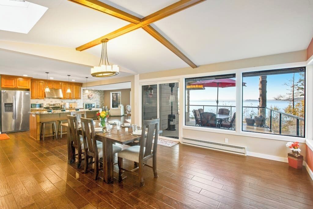 A spacious kitchen with modern appliances, a dining area with a wooden table and chairs, and large windows offering a view of the outdoors.