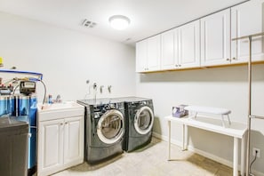 A laundry room with two front-loading washing machines, a sink, and a drying rack.