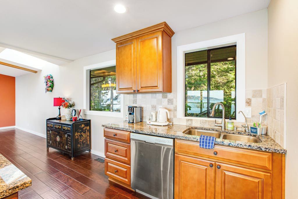A modern kitchen with wooden cabinets, a dishwasher, and a window providing a view of greenery outside.