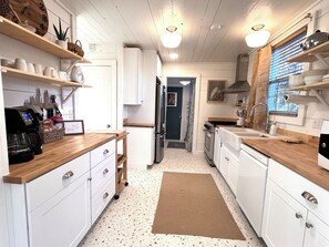 Een keuken met witte kasten, houten aanrecht, een koffiezetapparaat en een vloerkleed.