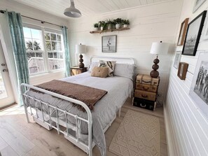 A bedroom with a bed, bedside tables, a window with curtains, wall-mounted shelves with plants, and a framed picture. - Stunning 1BR Oceanview -Patio -Washer Dryer- Hottub-Firepit (Moclips)
